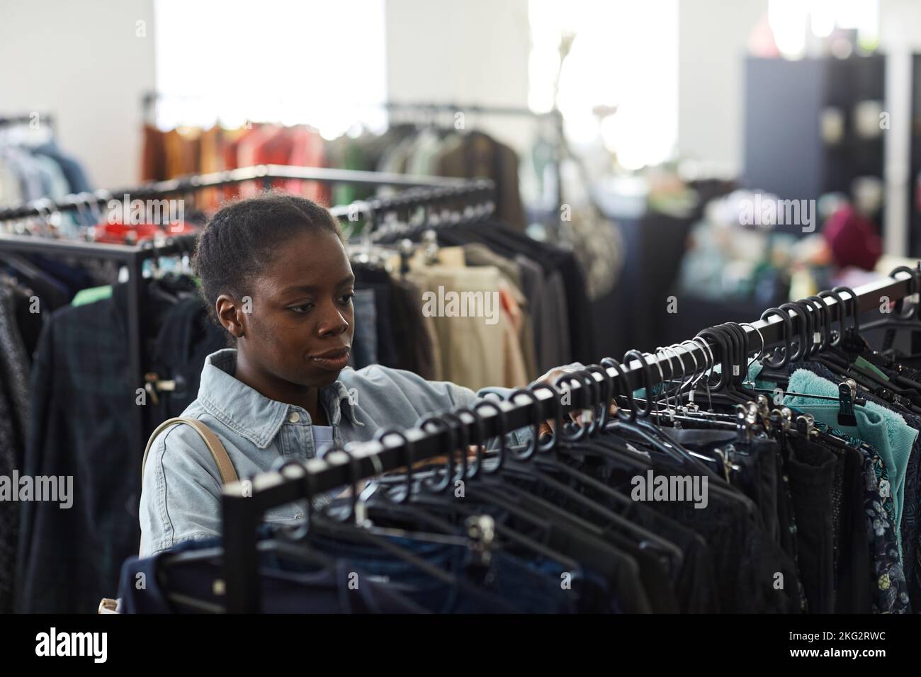 High angle portrait of black young woman looking at clothes on racks in thrift store Stock Photo