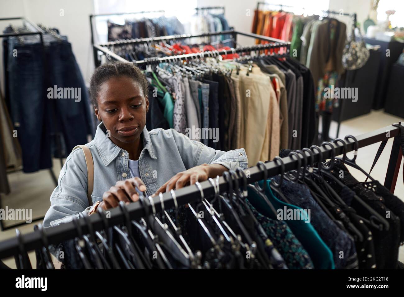 High angle portrait of black young woman looking at clothes while shopping for deals in thrift store Stock Photo