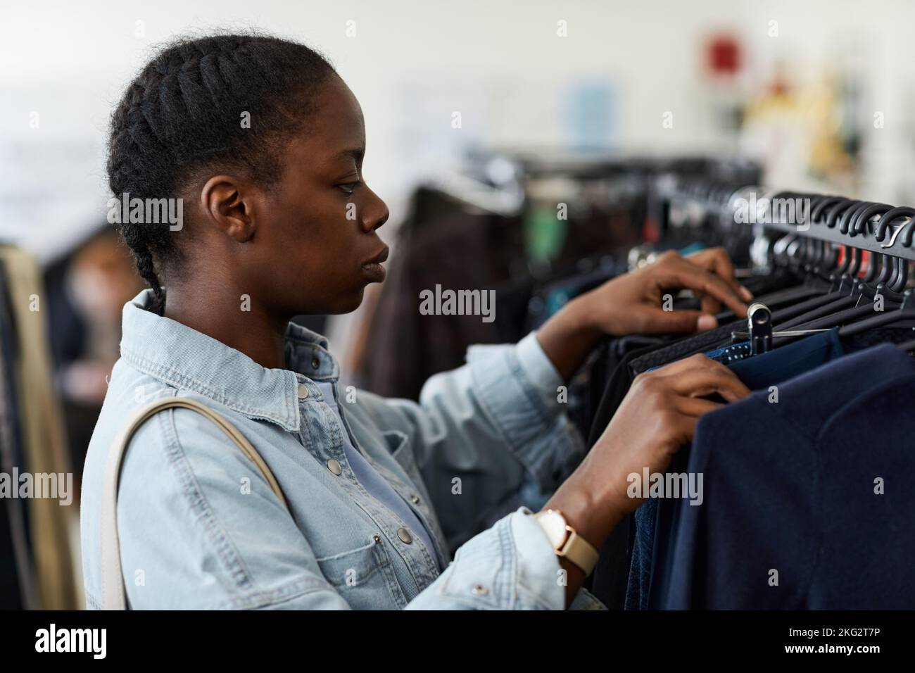 Side view portrait of black young woman browsing clothes on racks while shopping in thrift store Stock Photo