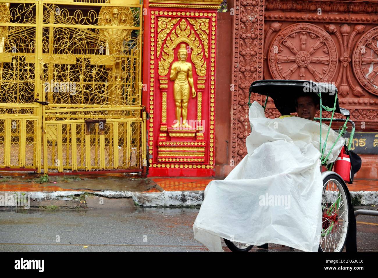 Cyclo driver wiating under the rain in front of a Pagoda. Phnom Penh. Cambodia. Stock Photo