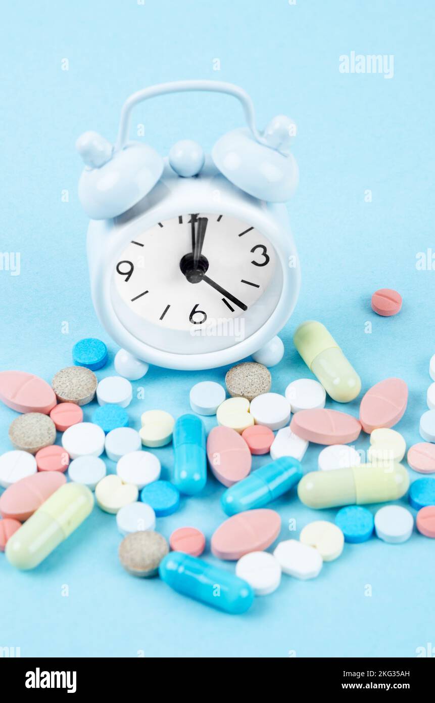 White alarm clock and many drug on a blue background. Taking medicine