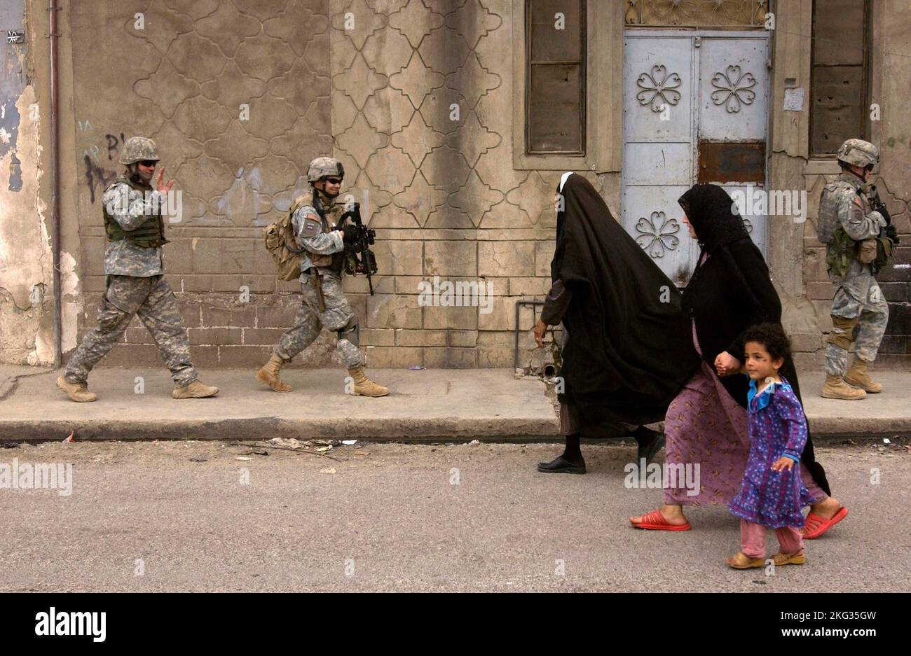 MOSUL, IRAQ - 12 April 2006 - US Army soldiers wave and smile as they pass by two Iraqi women and a child during a neighborhood foot patrol in Mosul, Stock Photo
