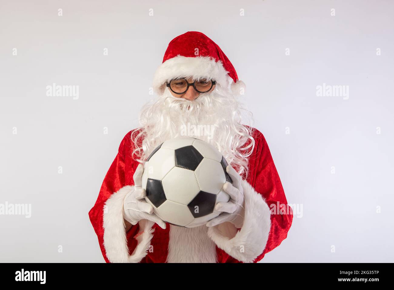 Santa Claus with glasses holding a World Cup soccer ball as a gift for all children, with a white background where his red suit and white beard stand Stock Photo