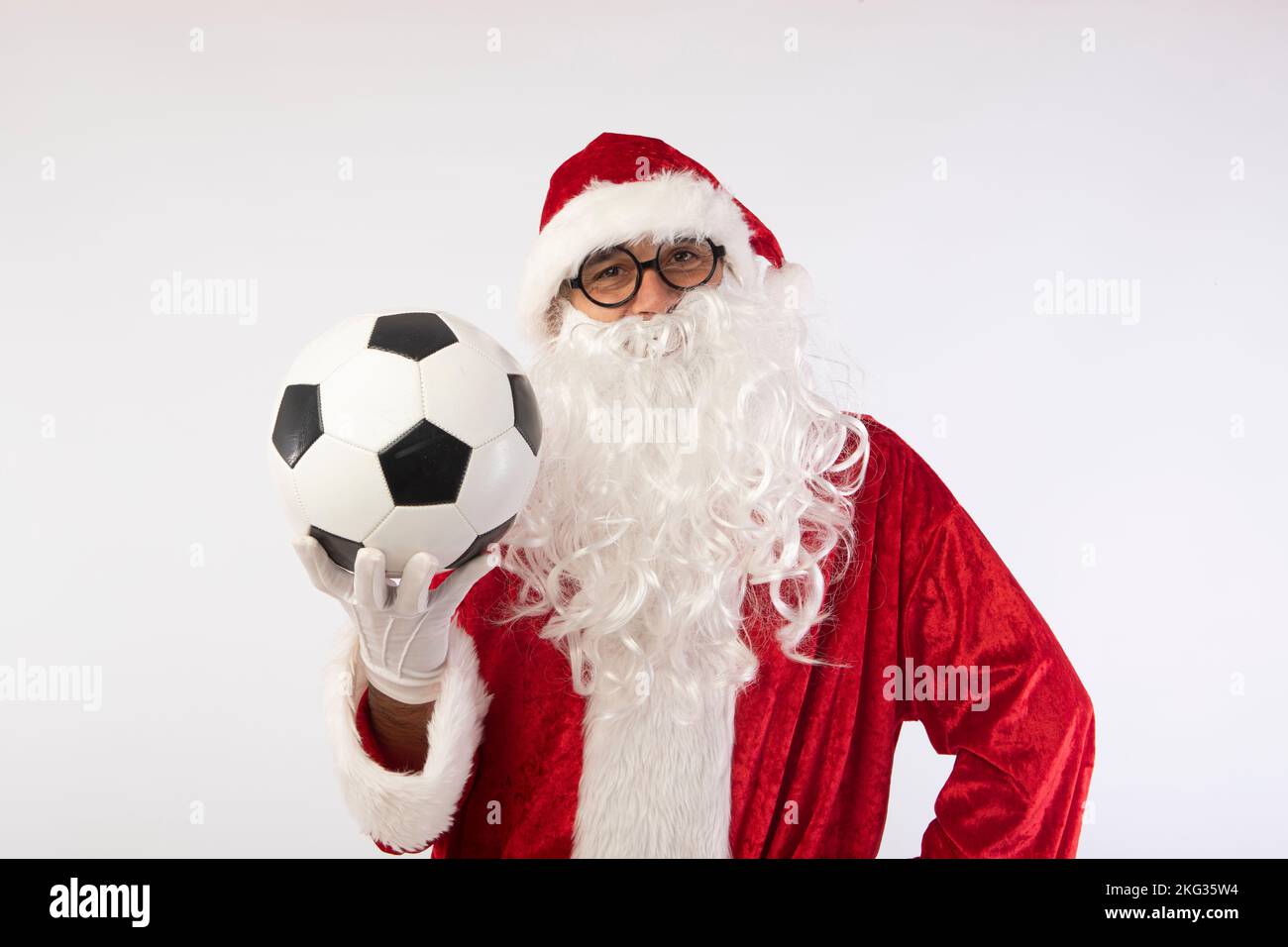 Santa Claus with glasses holding a World Cup soccer ball as a gift for all children, with a white background where his red suit and white beard stand Stock Photo