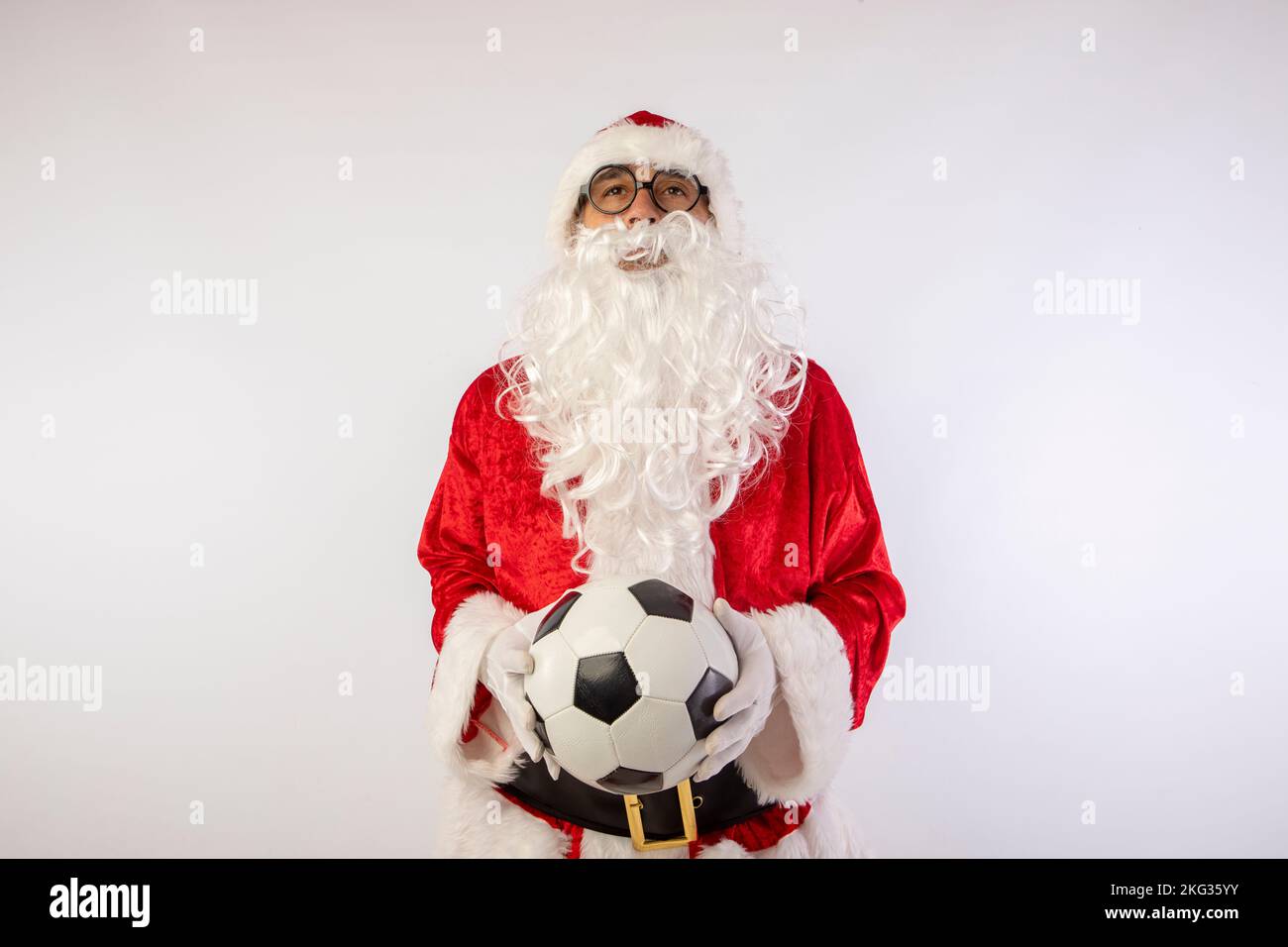 Santa Claus with glasses holding a World Cup soccer ball as a gift for all children, with a white background where his red suit and white beard stand Stock Photo