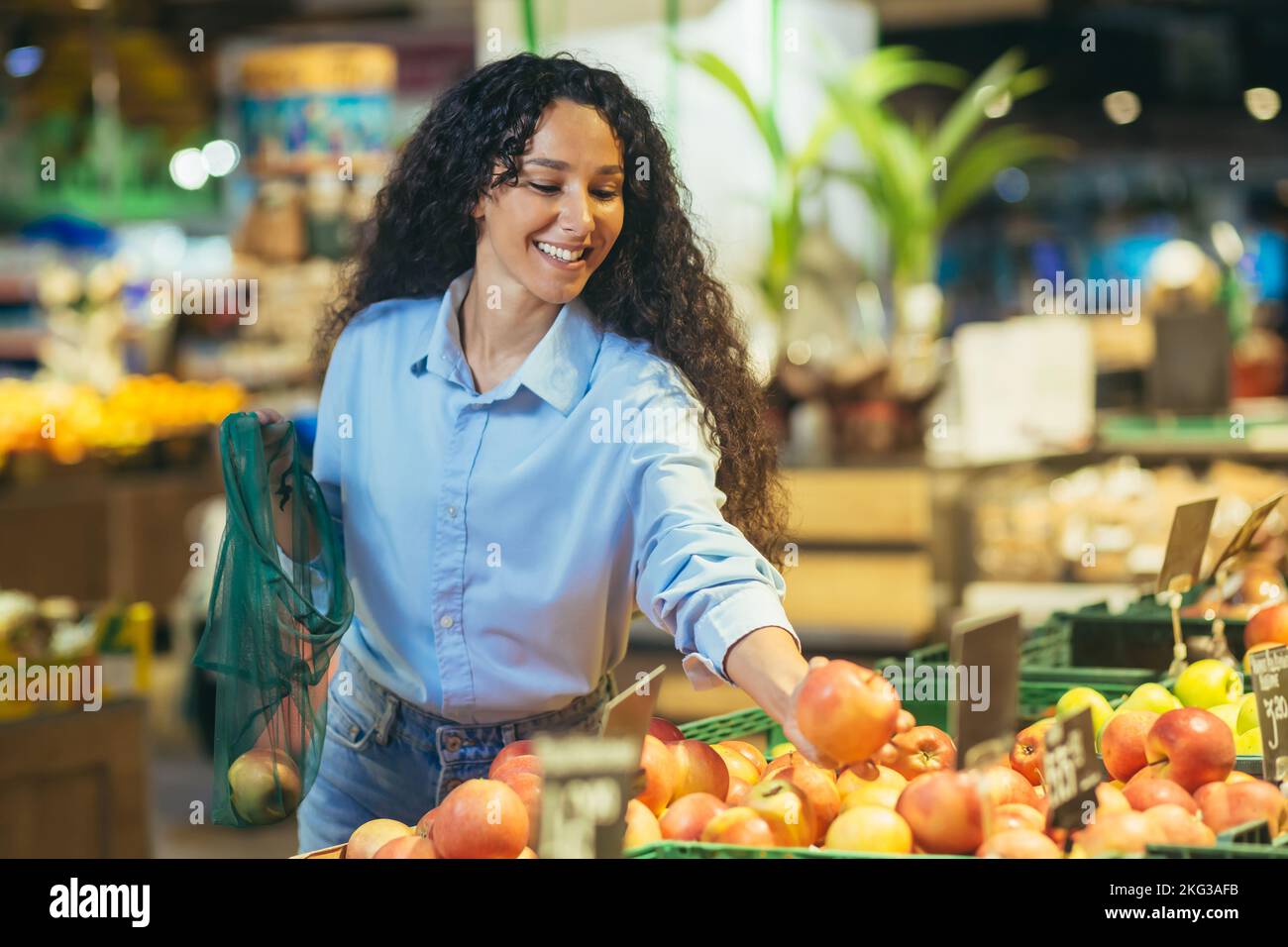 Happy woman buyer in supermarket, Latin American woman buys apples, fruits and vegetables, puts in an ecological bag. Stock Photo