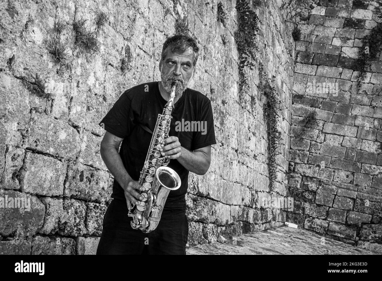 A musician playing trombone in front of stone wall on Crete Greece Stock Photo
