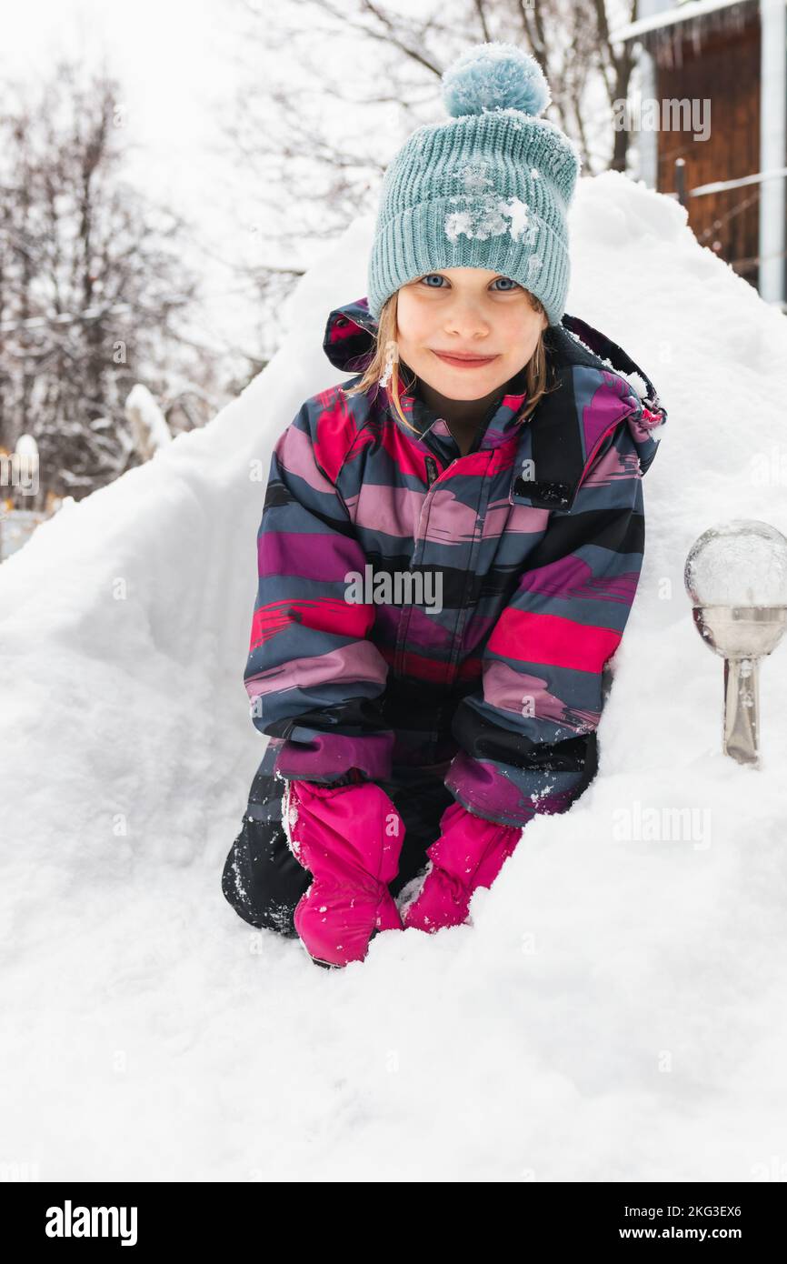 Happy little girl sitting in a snowdrift looking at camera smiling Stock Photo
