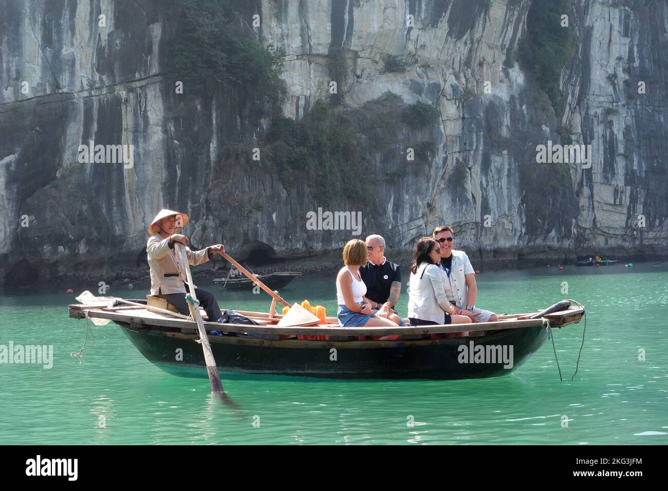 Tourist see the sights from a traditional wooden rowing boat courtesy of a local floating village resident in Halong Bay, Vietnam Stock Photo