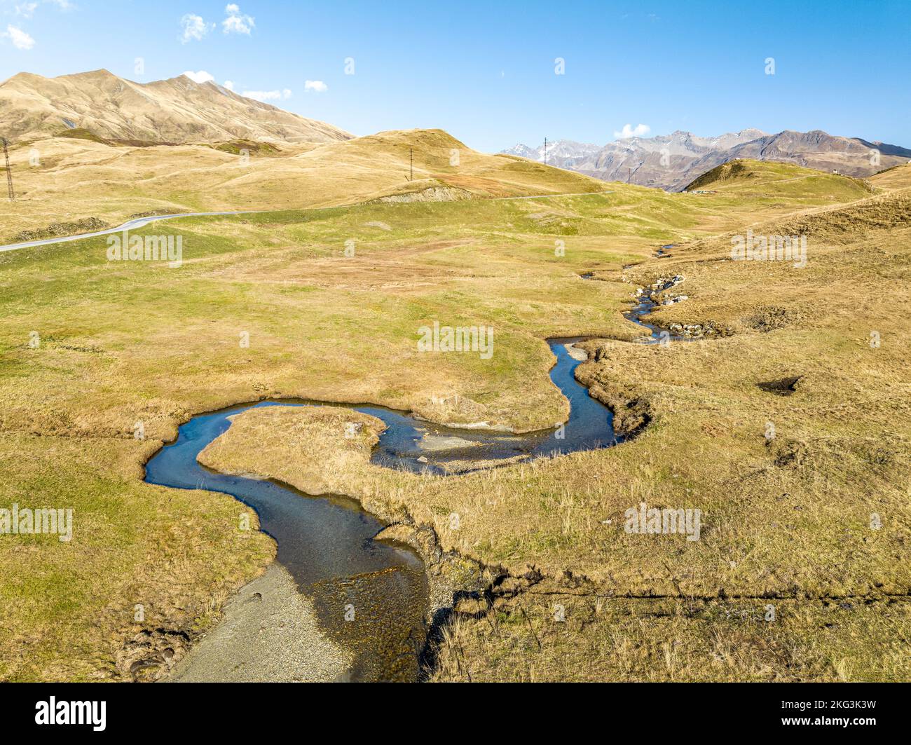 Mesmerising Panoramic perspective of lush grasslands at edge of  alpine mountain range featuring heartwarming water spring flowing in serpiant shape. Stock Photo