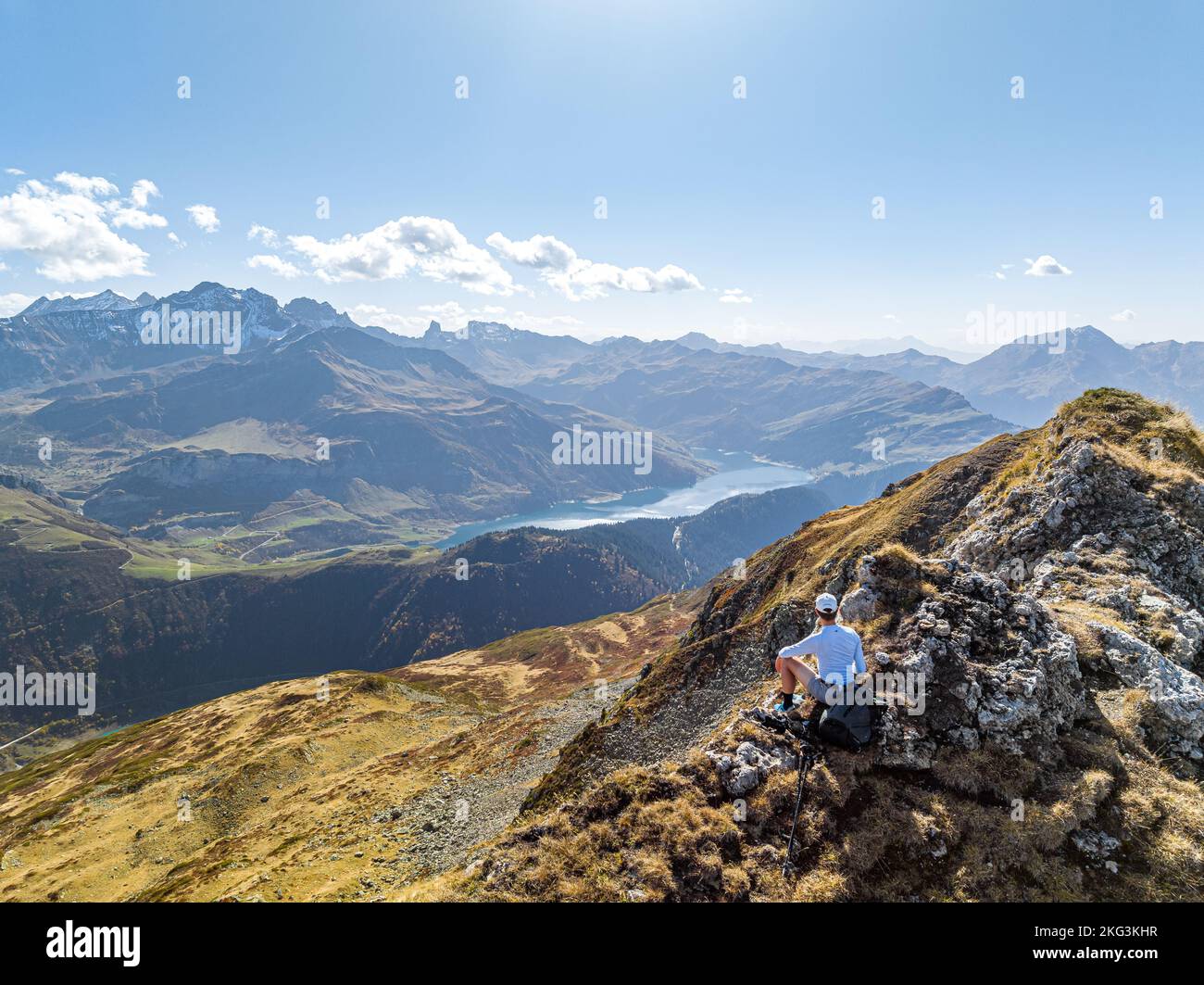 Aerial view of alone traveler relaxing while sitting on rock, staring at mountains alpine pastures in eastern France Stock Photo