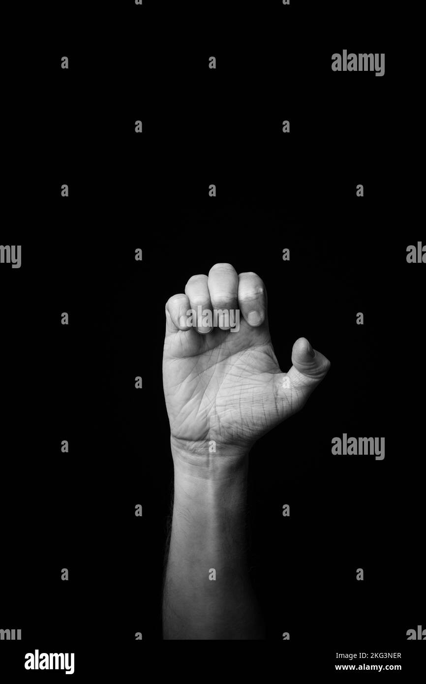 Dramatic black and white  image of a male hand fingerspelling the Fench sign language letter 'E', isolated against a dark background with copy space Stock Photo