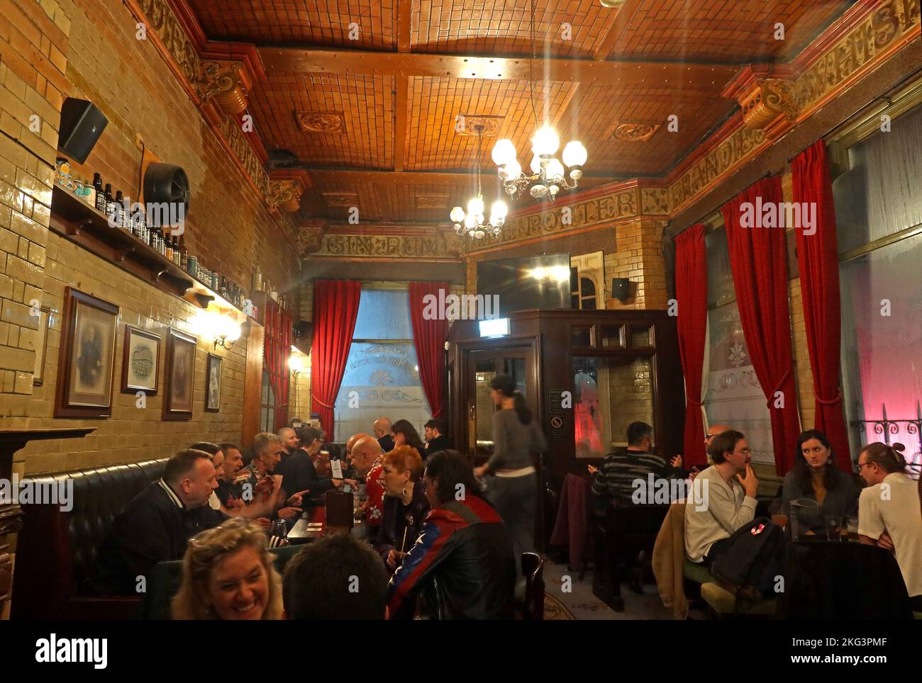 Customers socialise over real ale & craft beer drinks,beneath the ornate tiled ceiling inside Manchester's Grade II listed Marble Arch Inn at dusk Stock Photo
