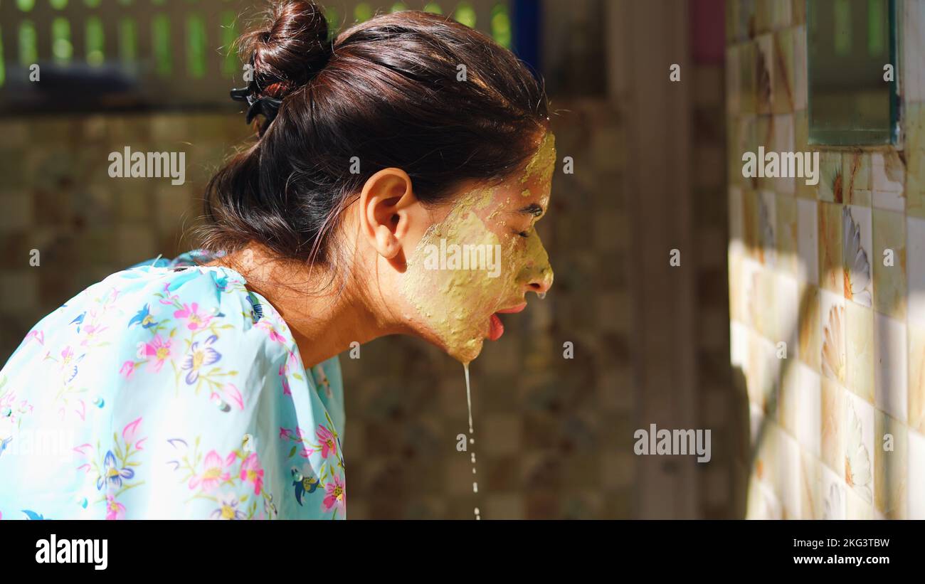 Beautiful woman is washing facial mask in bathroom after applying face mask. Girl spraying water on her face standing in front of mirror at home. mud Stock Photo