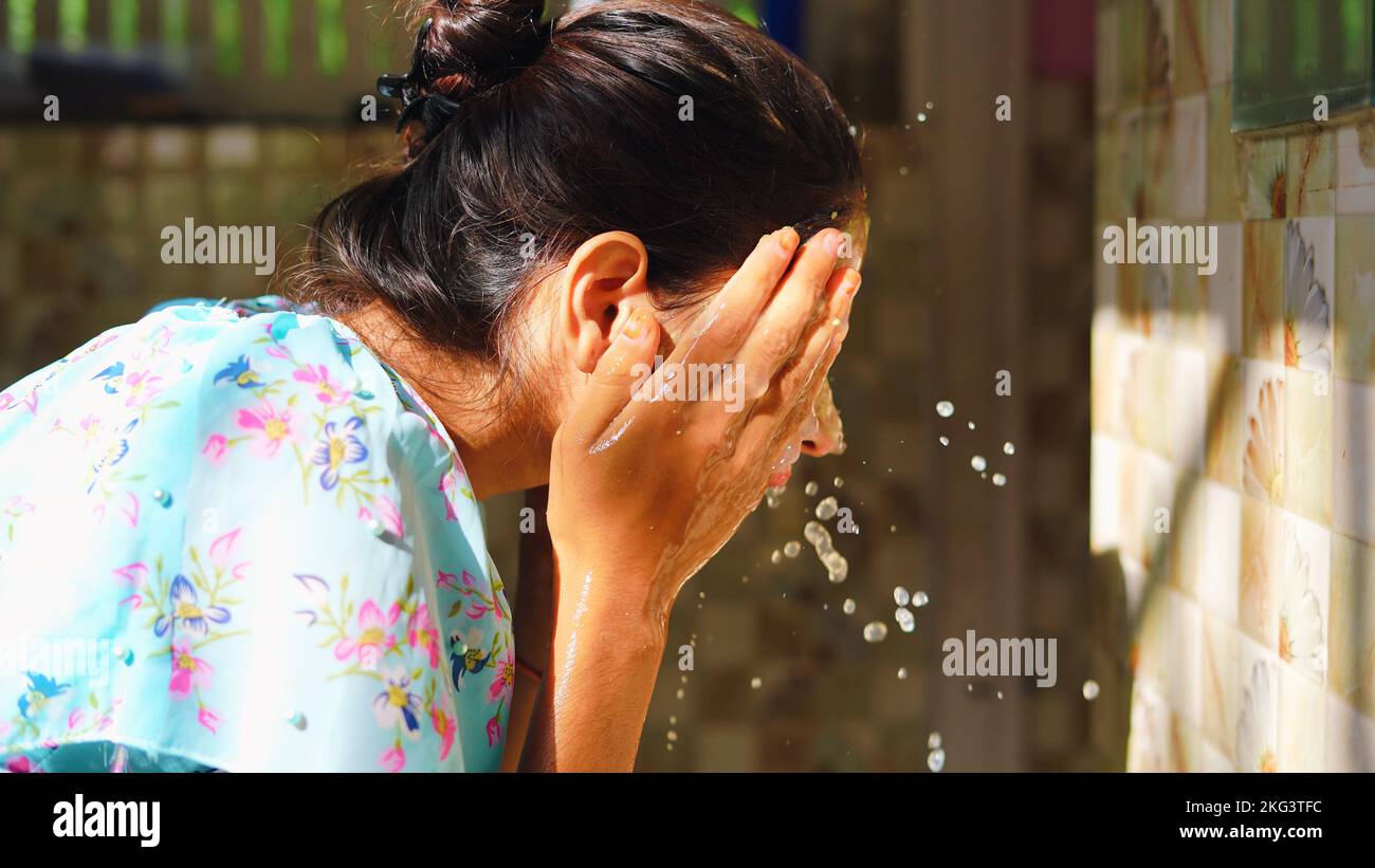 Beautiful woman is washing facial mask in bathroom after applying face mask. Girl spraying water on her face standing in front of mirror at home. mud Stock Photo