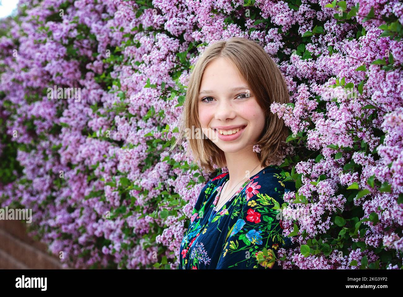 Pretty blond teen girl surrounded by lilac blooms. Stock Photo