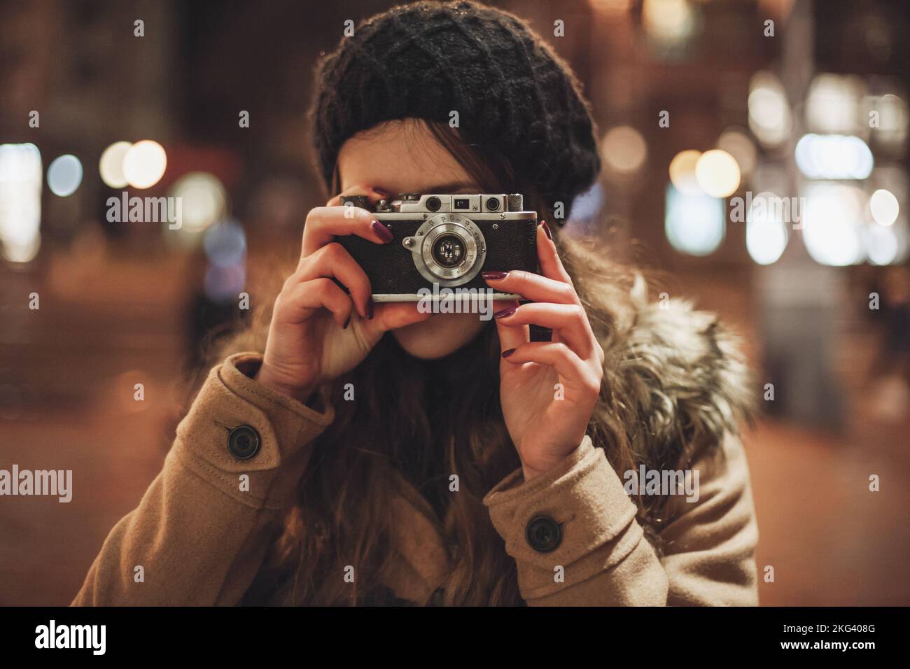 Hipster girl with retro camera taking photos in the night city street Stock Photo