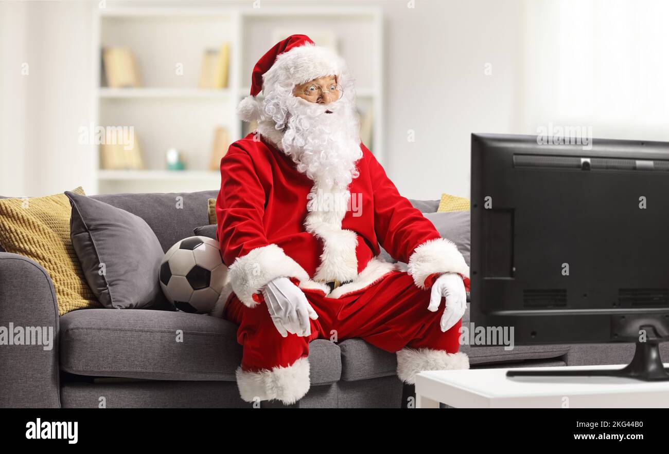 Excited santa claus sitting on a sofa and watching football on tv at