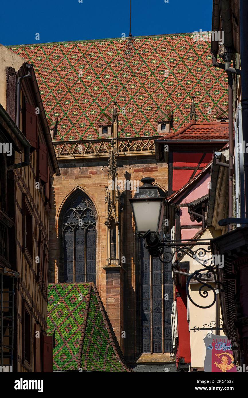 Burgundian-style polychrome roofs with glazed tiles laid in geometric patterns surmount walls and Gothic pinnacles in pink Vosges sandstone on the south side of the Église Saint-Martin, built between 1235 and 1365 in the historic heart of Colmar, Alsace, Grand Est, France, as a collegiate foundation dedicated to St Martin of Tours. Stock Photo