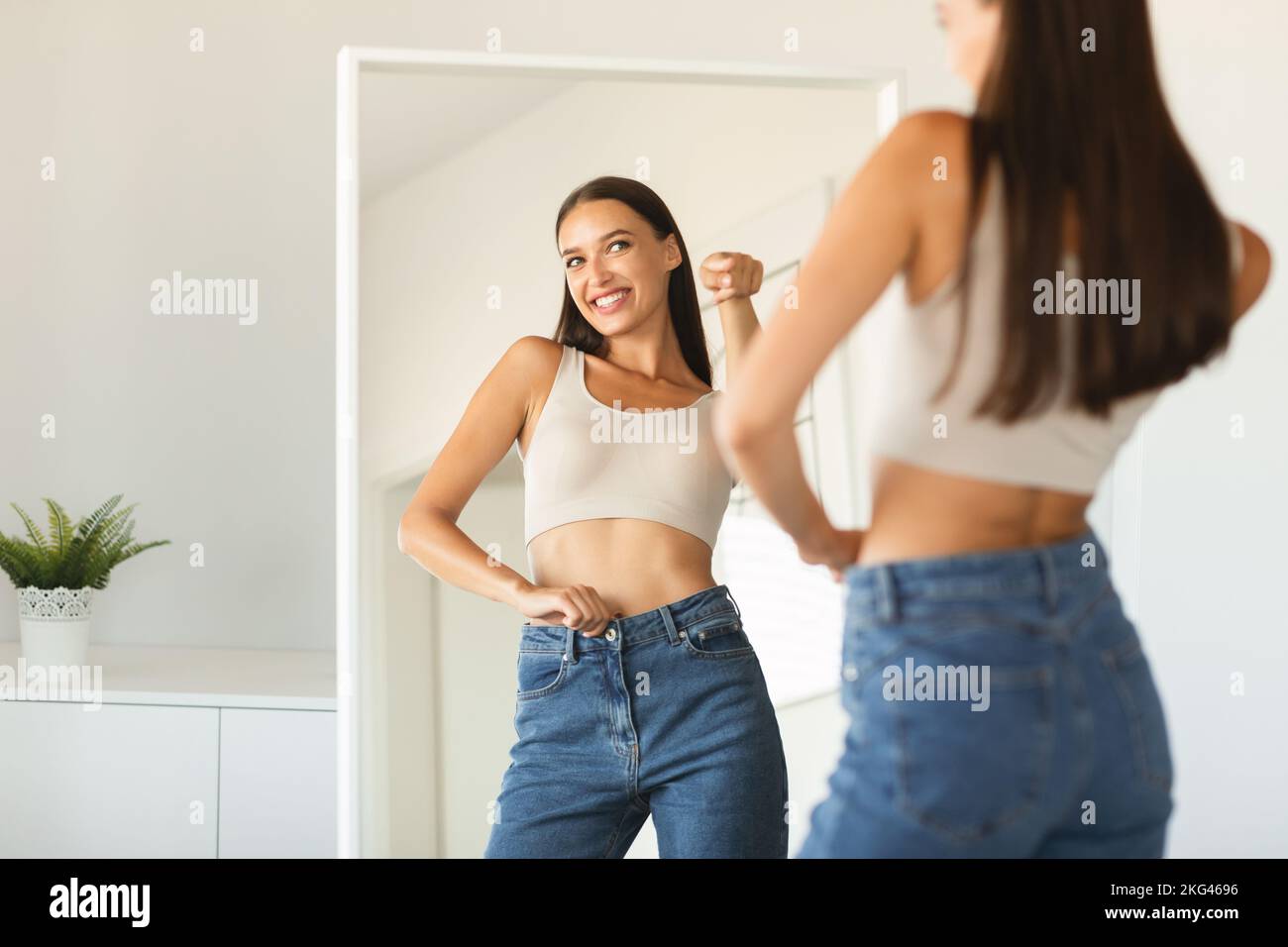 Self confidence concept. Happy caucasian lady pointing finger at her reflection in mirror, posing after weight loss Stock Photo