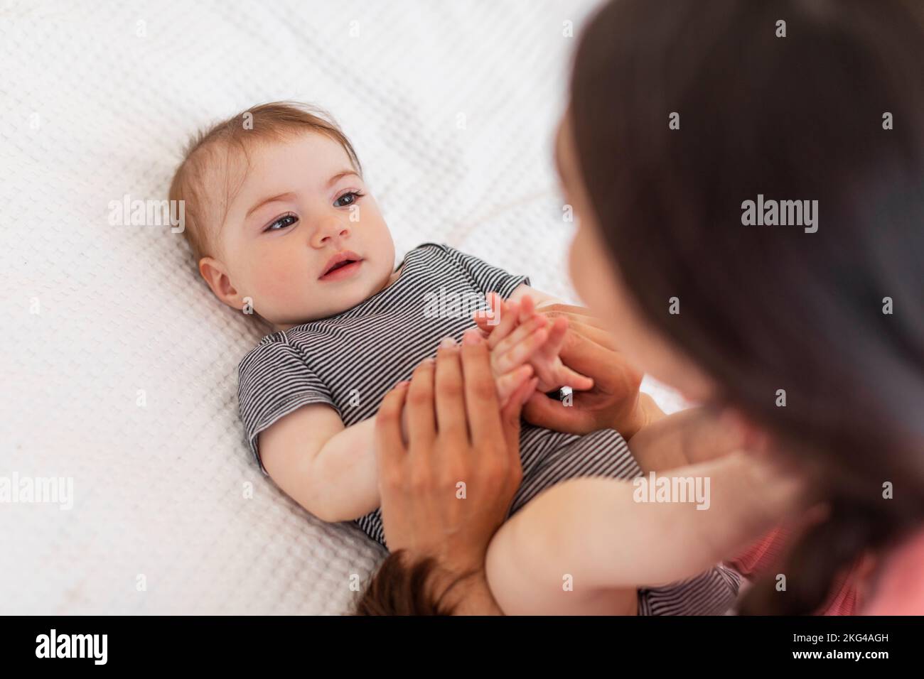 Good morning sunshine. Adorable little baby lying on bed and looking at mother, caring mom holding child's hands Stock Photo