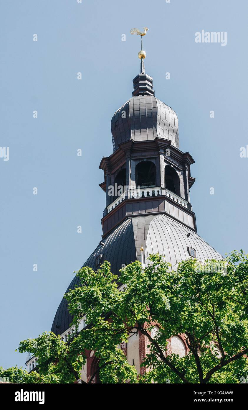 church tower with a green metal roof and a balcony topped with a gilded rooster under a blue sky. Stock Photo