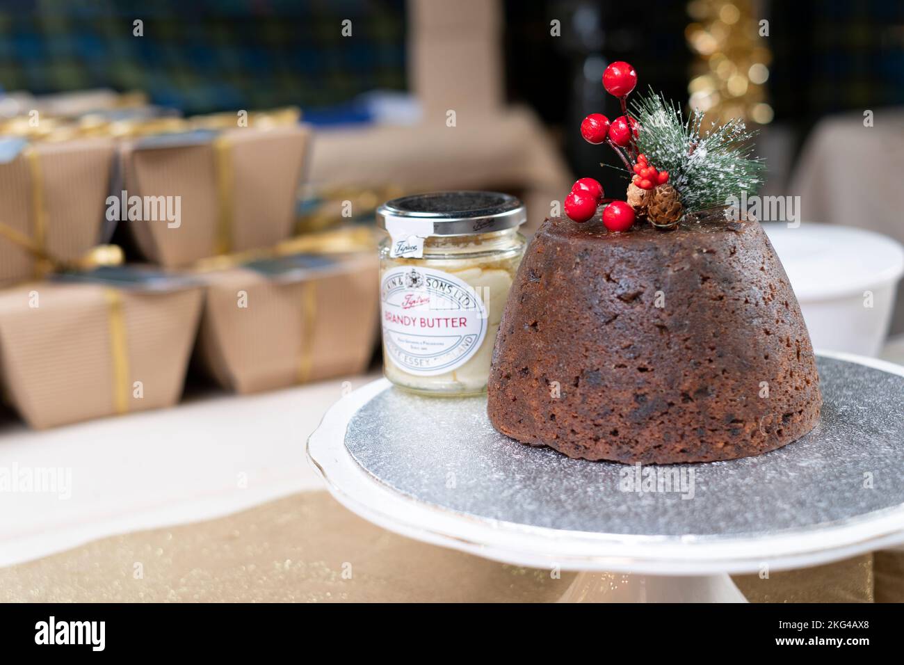 A traditional fresh Christmas pudding  with a jar of Brandy Butter. The pudding decorated with festive berries and a sprig of frosted pine leaves Stock Photo