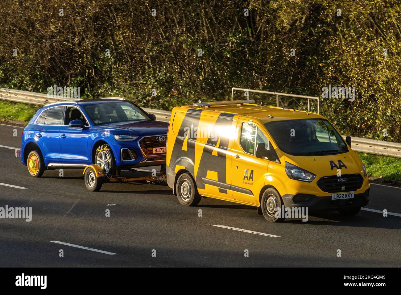 AA rescue vehicle or van towing a broken down car on a trailer along the M3 motorway, England, UK. Automobile Association, breakdown organisation Stock Photo