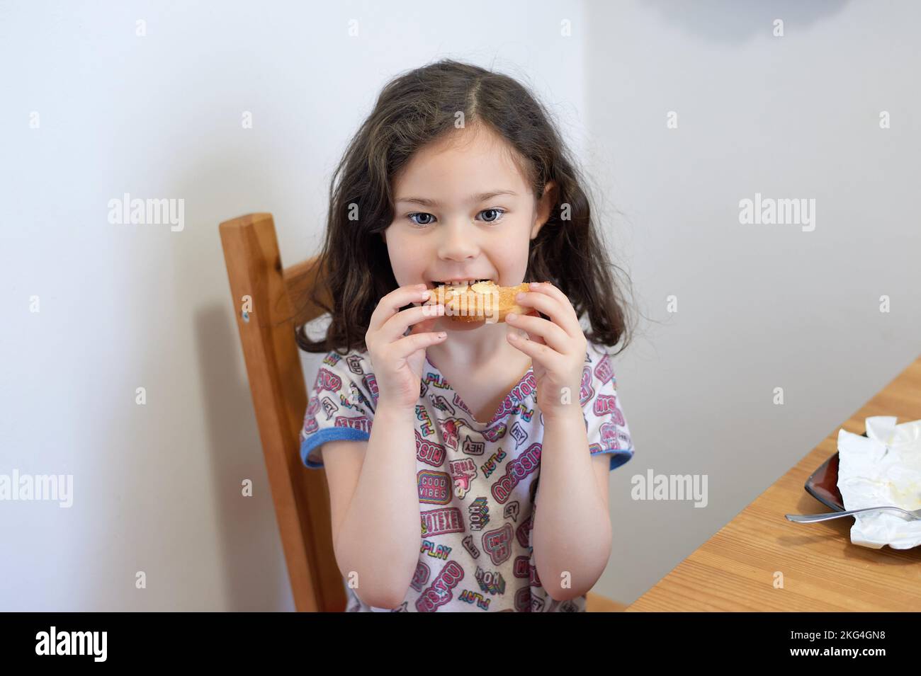 Young girl eating toast with butter at the kitchen table for breakfast ...