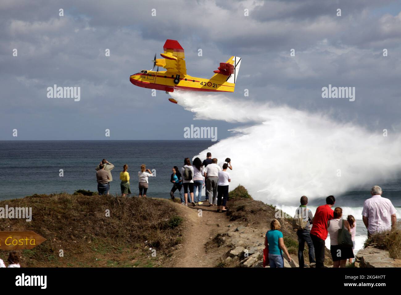 Small firefightermen plane throwing water in front of the coast with people watching it. Playa de las Catedrales, Galicia, Ribadeo, Lugo, Spain. Stock Photo