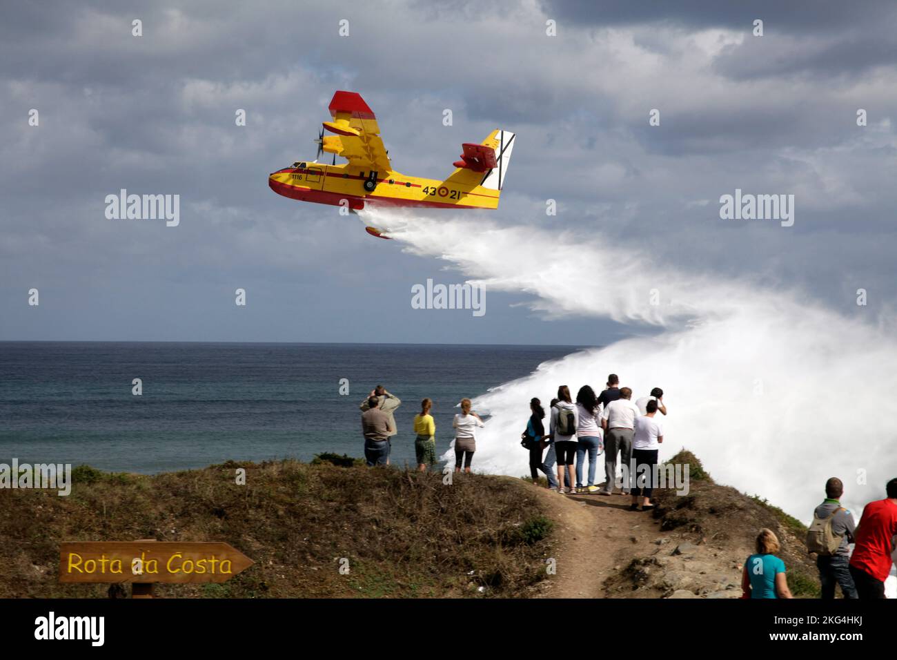 Small firefightermen plane throwing water in front of the coast with people watching it. Playa de las Catedrales, Galicia, Ribadeo, Lugo, Spain. Stock Photo