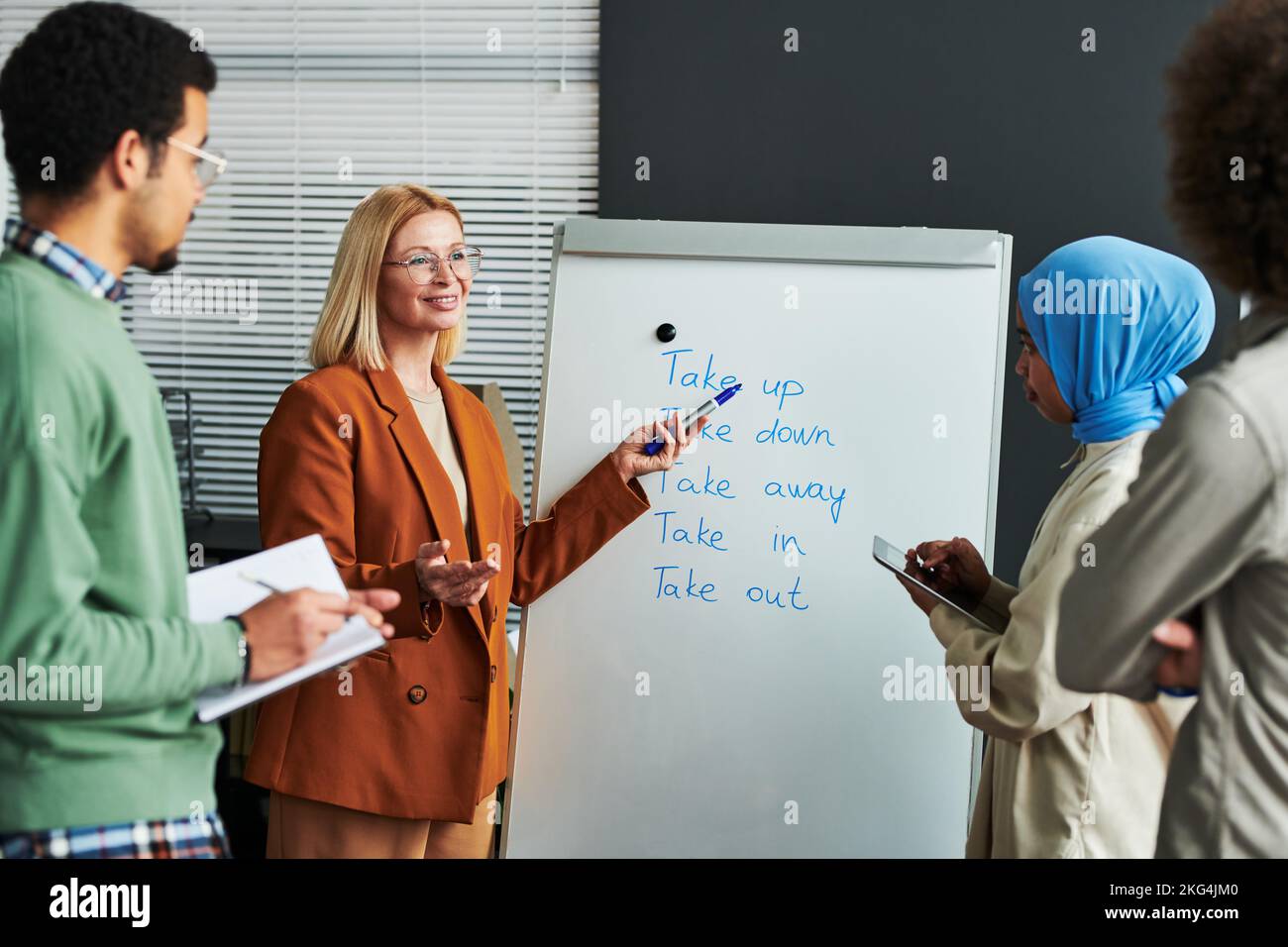 Confident mature teacher of English language pointing at whiteboard