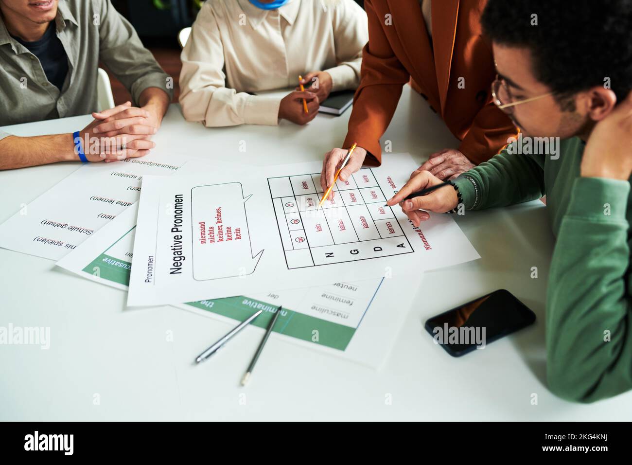 Group of students gathered by table at lesson of German grammar while mature teacher of foreign languages explaining negative pronouns Stock Photo