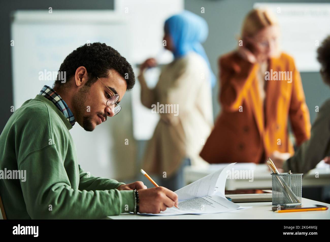 Young serious student in eyeglasses and casual pullover making notes on paper with exam text during individual work at lesson Stock Photo