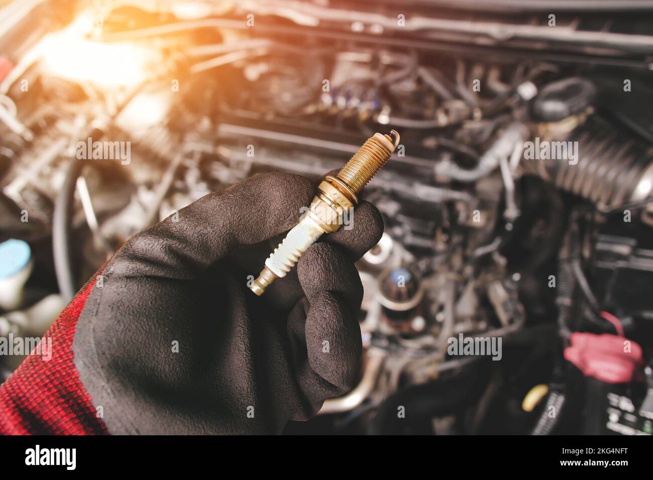 Automobile iridium spark plugs holds by auto mechanic hand with engine compartment blurred background and sunlight. Stock Photo