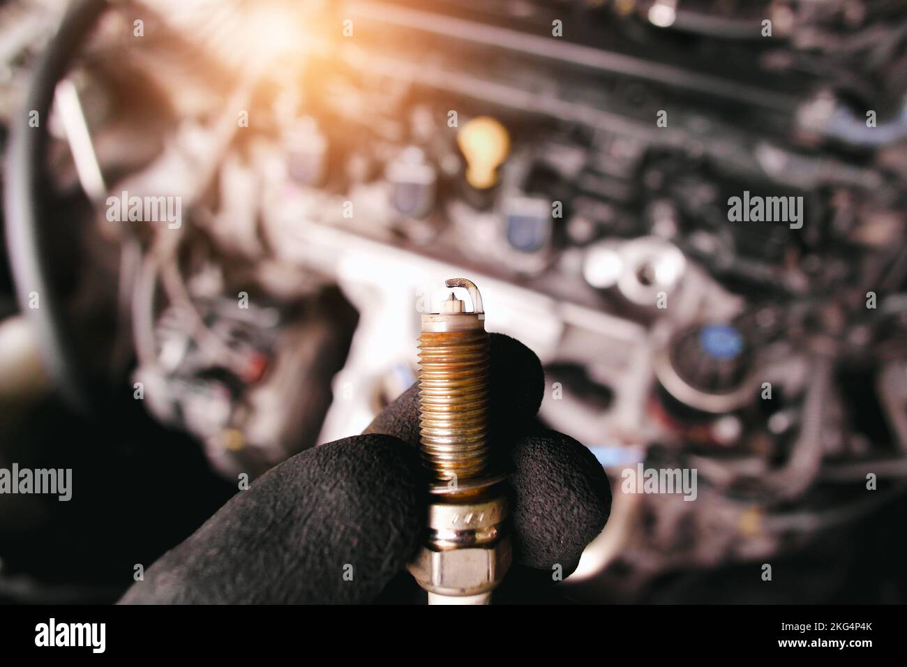 Close up of car iridium spark plugs damaged by heavy use of the car engine ignition system, engine compartment blurred on background with sunlight Stock Photo