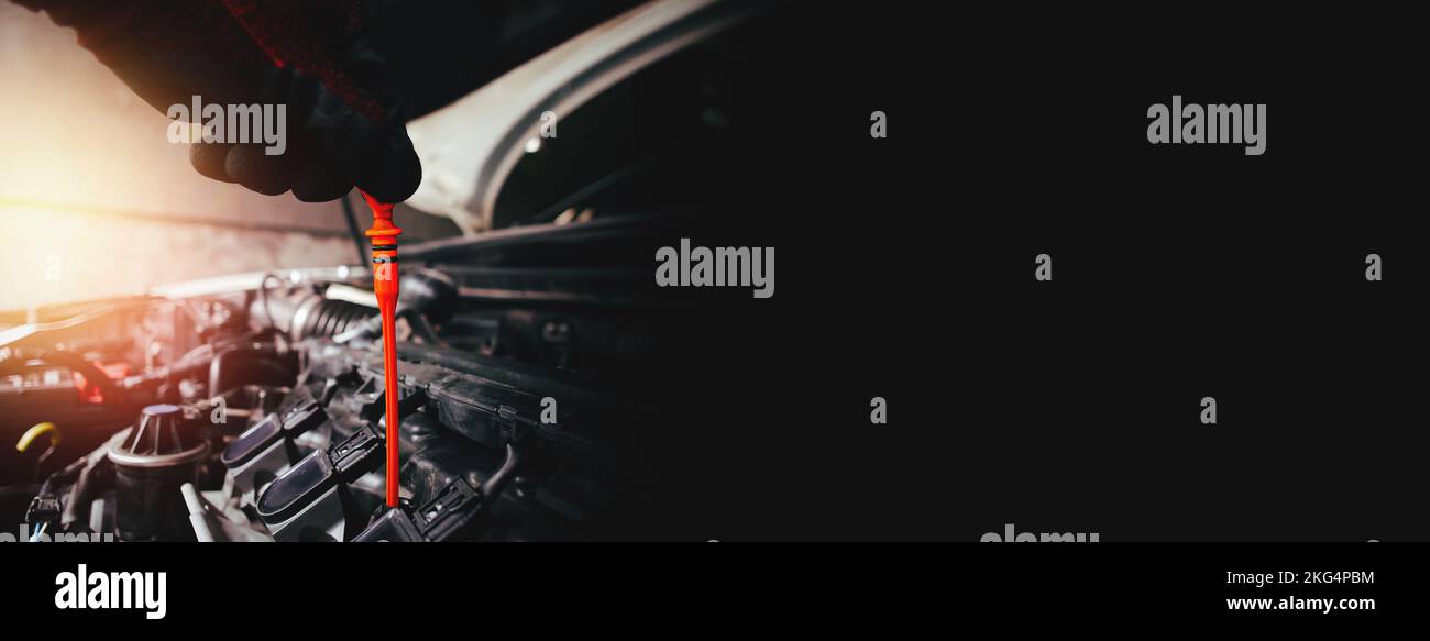 A auto mechanic is pulling the orange dipstick to check the motor oil level of the combustion