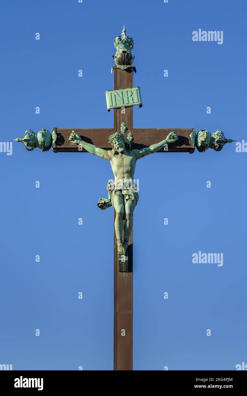 Ancient landmark crucifix monument, weathered bronze statue of Jesus Christ on the Cross isolated against bright blue sky, Montpellier, France Stock Photo