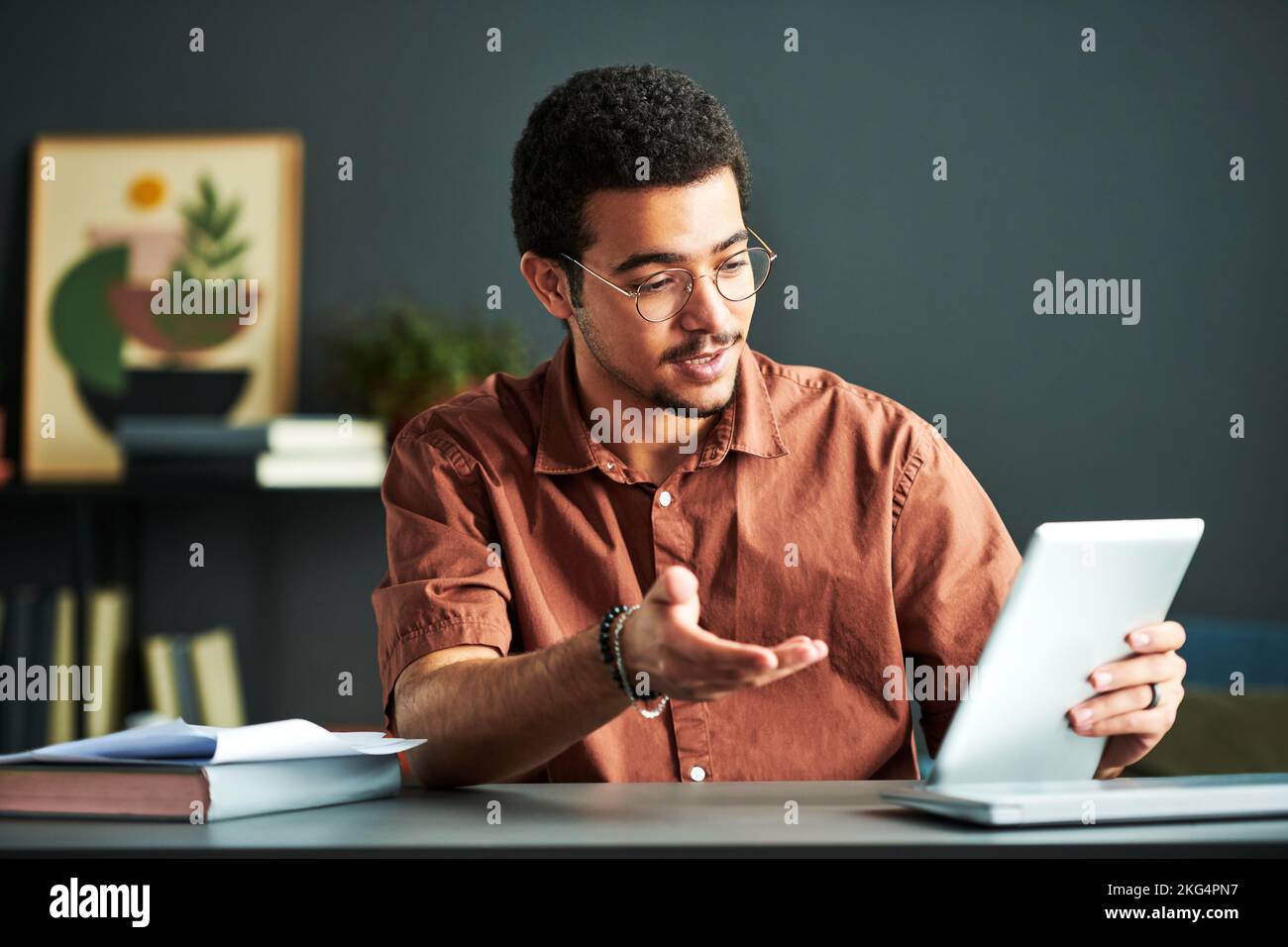 Young confident tutor in eyeglasses answering questions of online audience while looking at tablet screen during video lesson Stock Photo