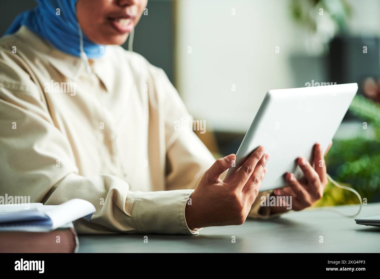 Hands of young Muslim tutor holding tablet in front of herself while communicating with online student or audience during online lesson Stock Photo