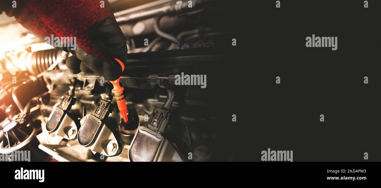 A mechanic is pulling the orange dipstick to check the oil level of the combustion engine in the