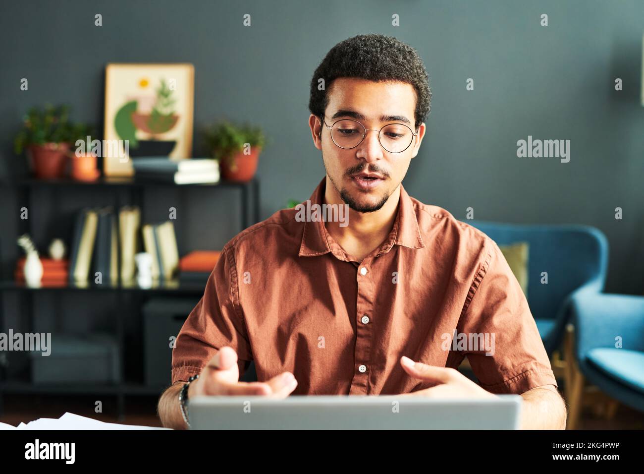 Young businessman or online student or tutor communicating with online audience while sitting by workplace in front of laptop Stock Photo