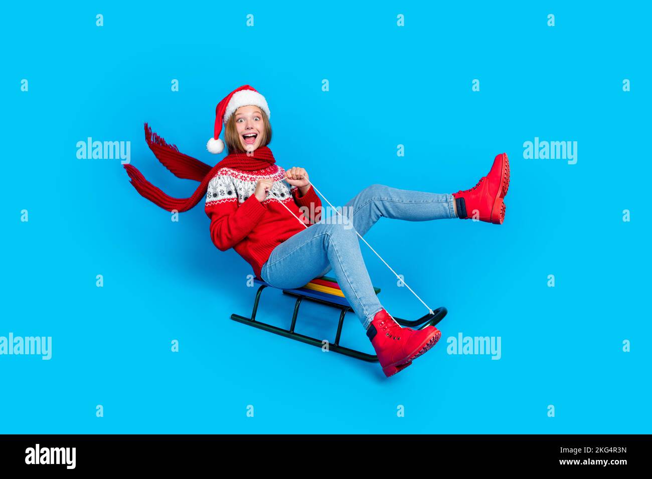 Full length photo of funky impressed school girl dressed red x-mas ornament pullover riding sledges fast isolated blue color background Stock Photo