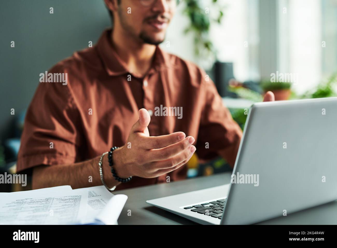 Focus on hand of young male tutor or student explaining something during online lesson while sitting by desk in front of laptop screen Stock Photo
