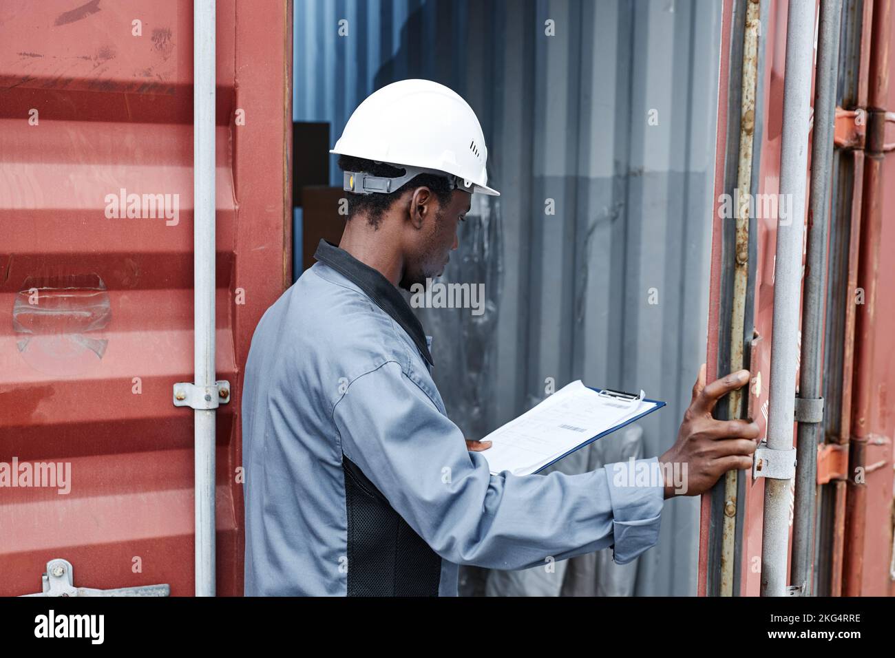 Back view of male worker wearing hardhat while checking containers at shipping dock, copy space Stock Photo