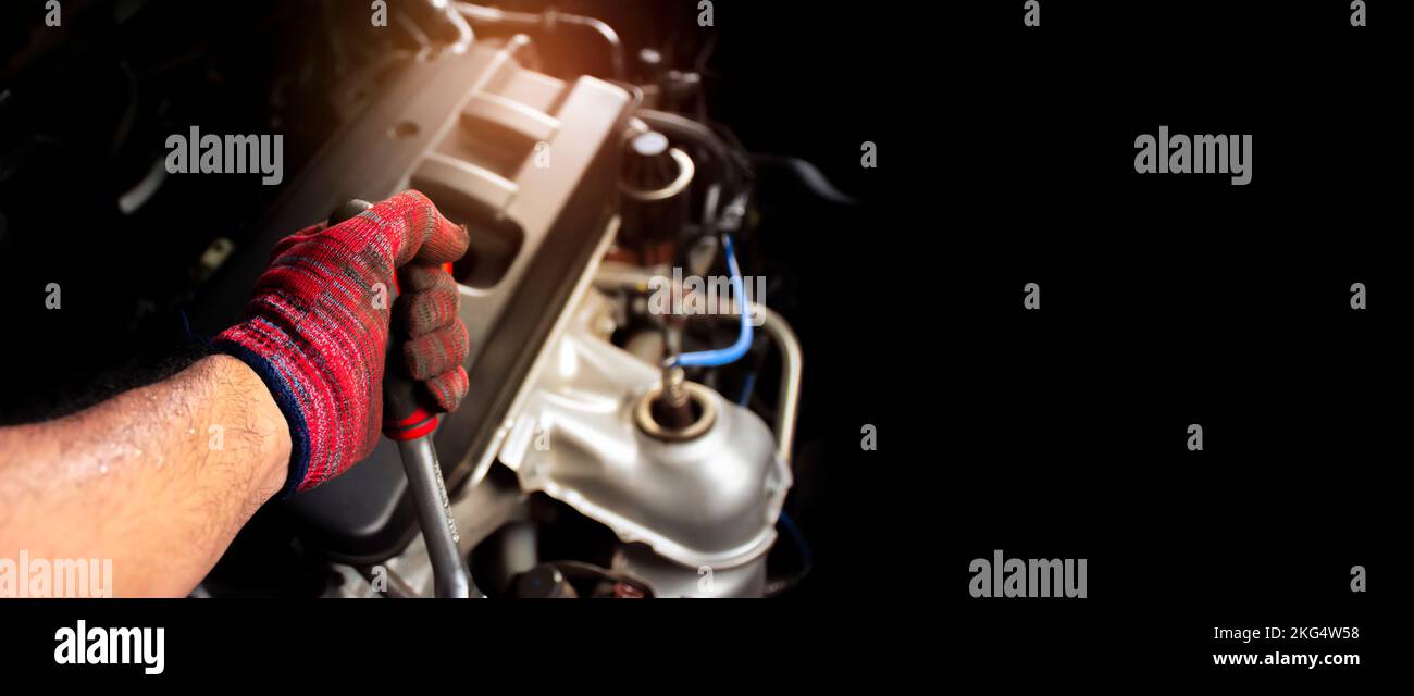 A mechanic is using a socket wrench to fix a broken car engine in the