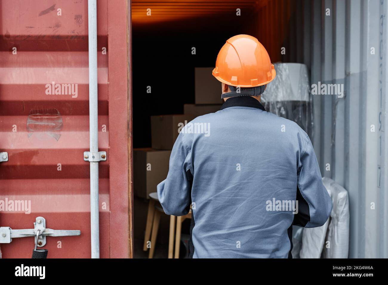 Graphic back view of worker wearing hardhat checking containers at shipping dock, copy space Stock Photo