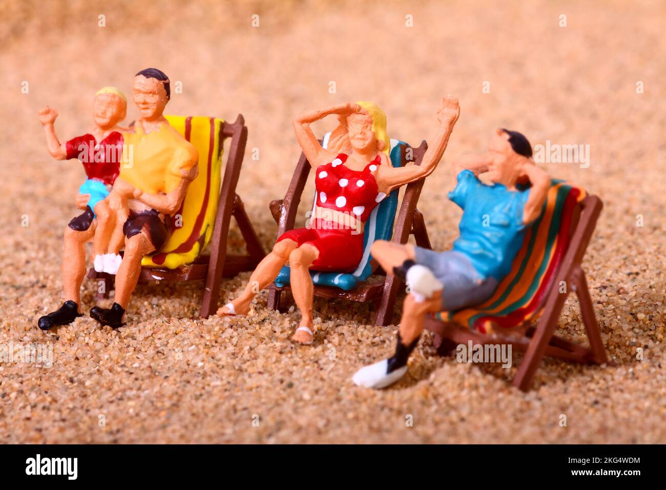 Conceptual image of miniature figure people sat on deck chairs on a sandy beach, Holiday vacation concept Stock Photo