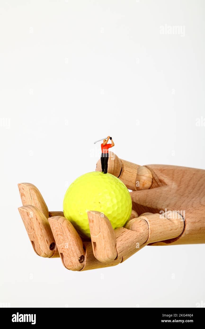Conceptual image of a miniature figure golfer teeing off from a golf ball held in a wooden hand Stock Photo