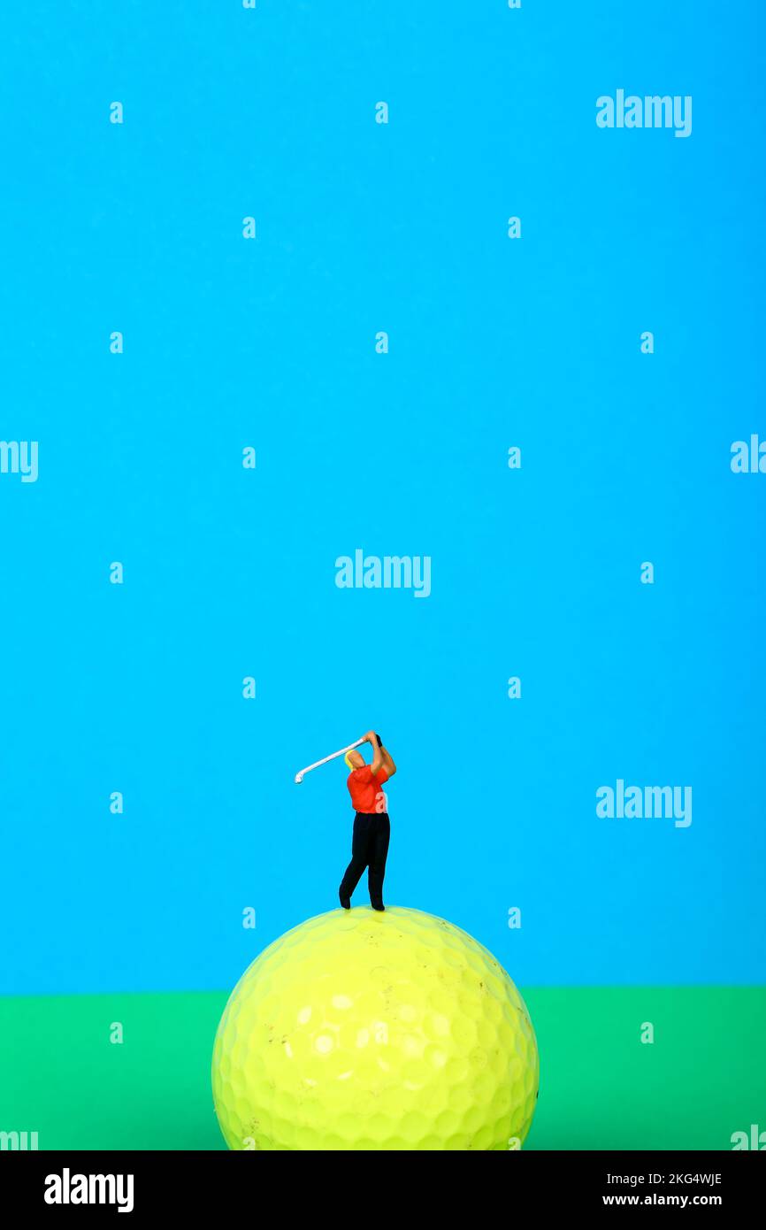 Conceptual image of a miniature figure golfer teeing off from a golf ball Stock Photo